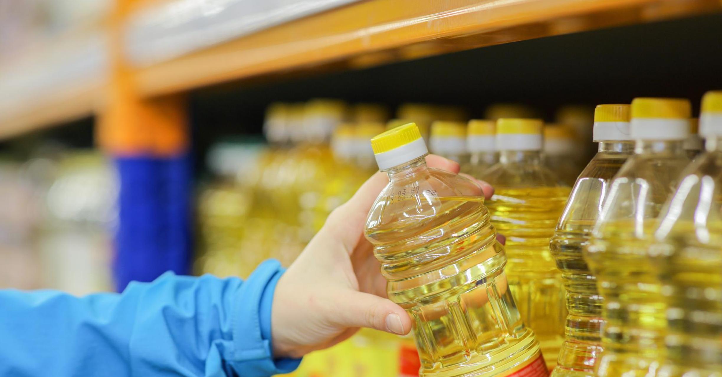 hand selecting a bottle of cooking oil from a supermarket shelf