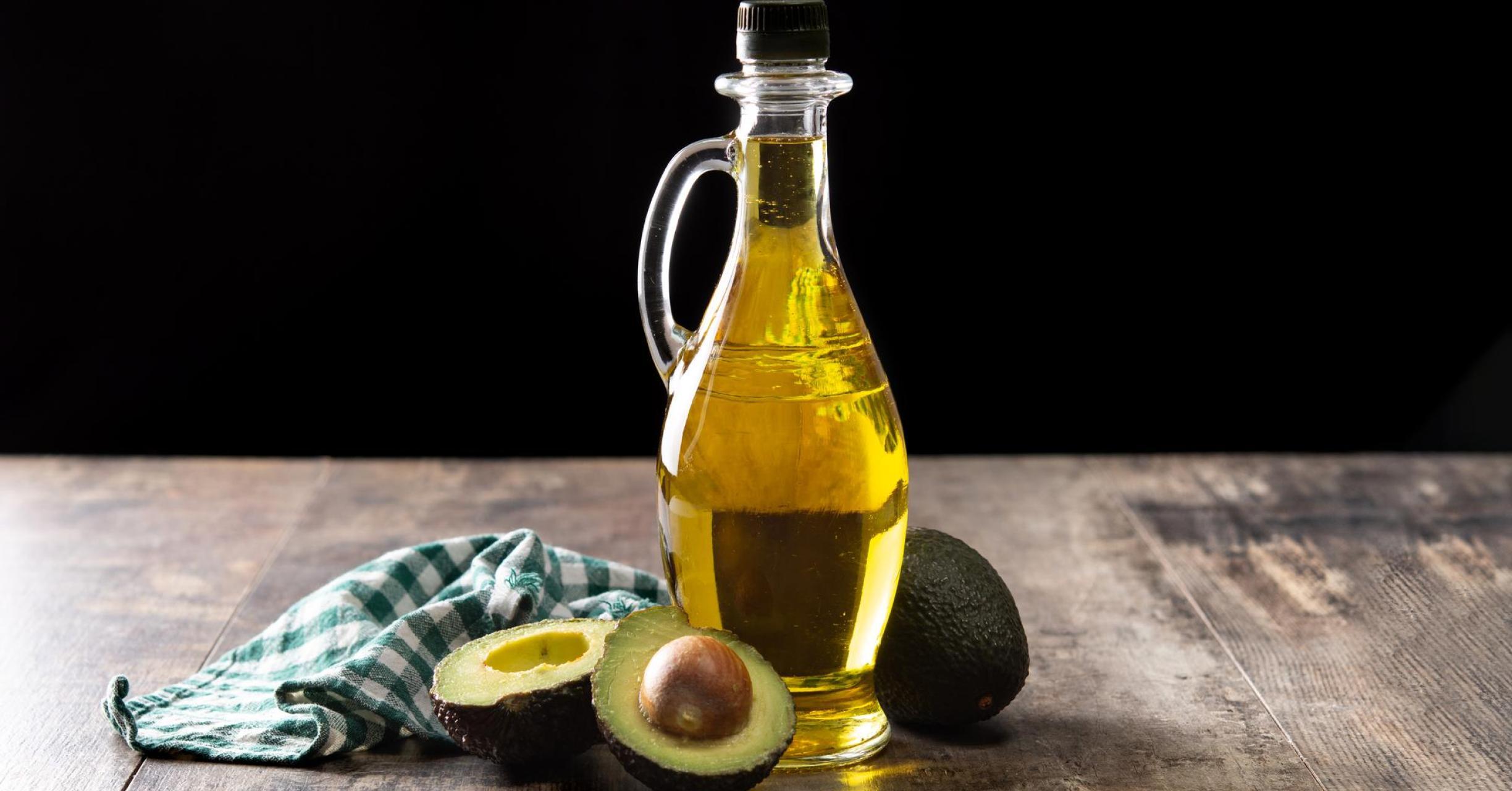 bottle of olive oil beside a halved avocado on a wooden surface
